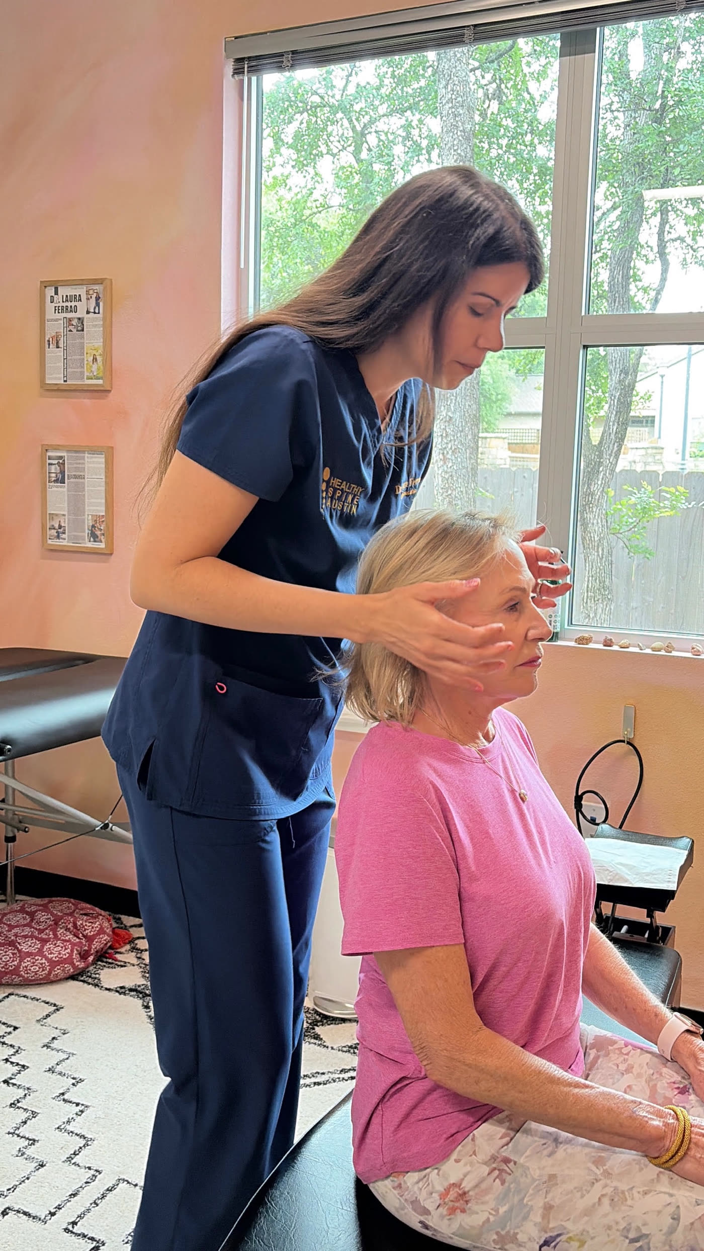 Dr. Laura's hands resting gently on a patient's head by a sunny window