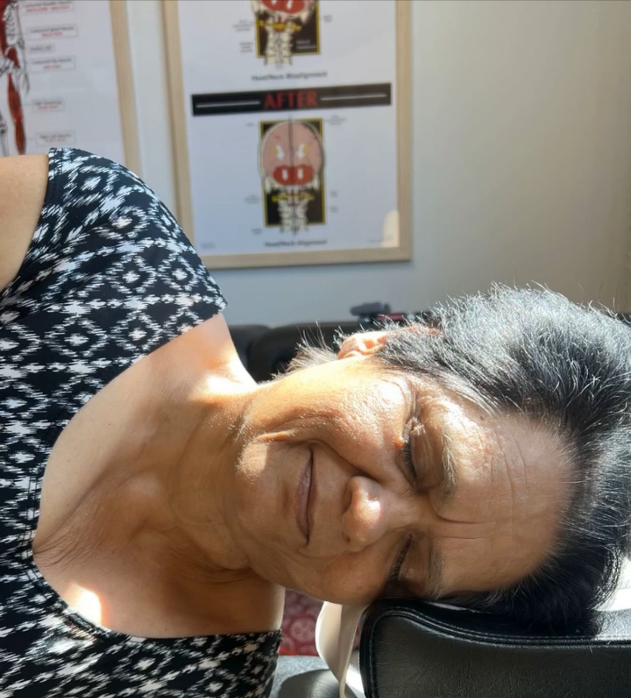 A patient smiling peacefully with her eyes closed as she rests on the adjusting table in warm sunlight